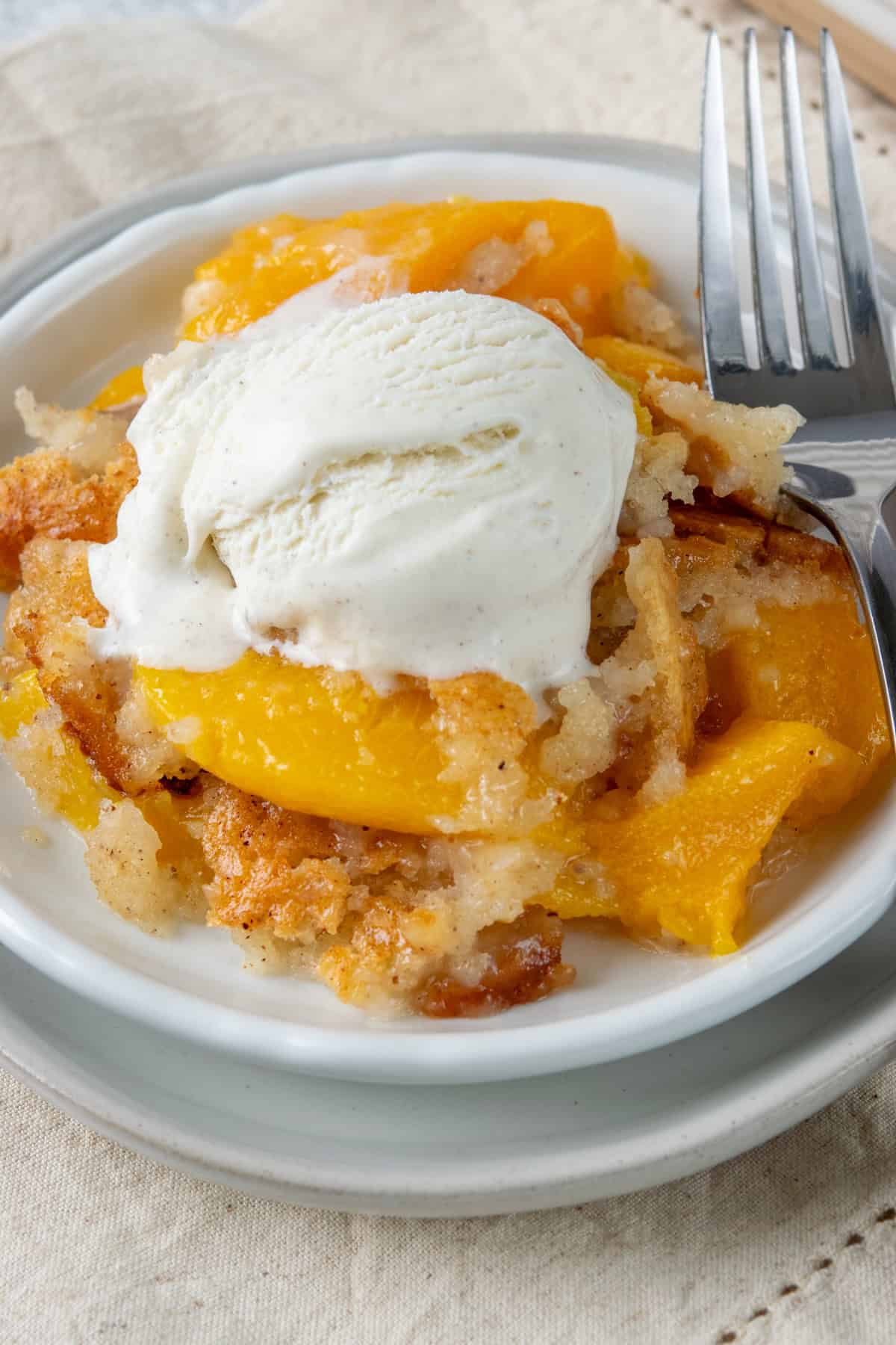 A rich serving of Bisquick peach cobbler topped with melting vanilla ice cream, featuring juicy peaches and a buttery golden cobbler.