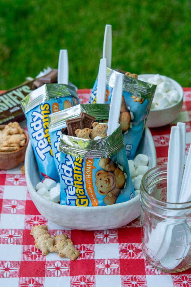 Three-photo collage showing walking s'mores assembly, including a close-up of chocolate pudding with marshmallows and Hershey's chocolate in a Teddy Grahams bag, plus the ingredients used to make the dessert.