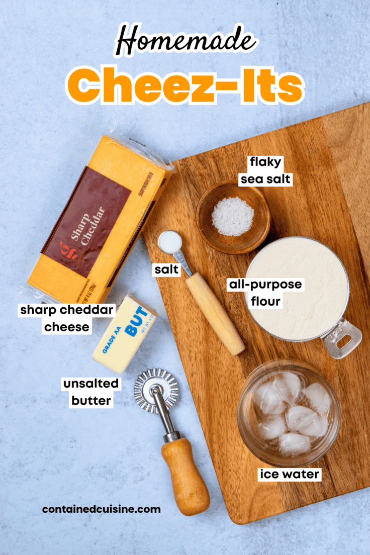 Ingredients for homemade Cheez-Its arranged overhead, including sharp cheddar cheese, flour, butter, salt, ice water, and flaky sea salt.