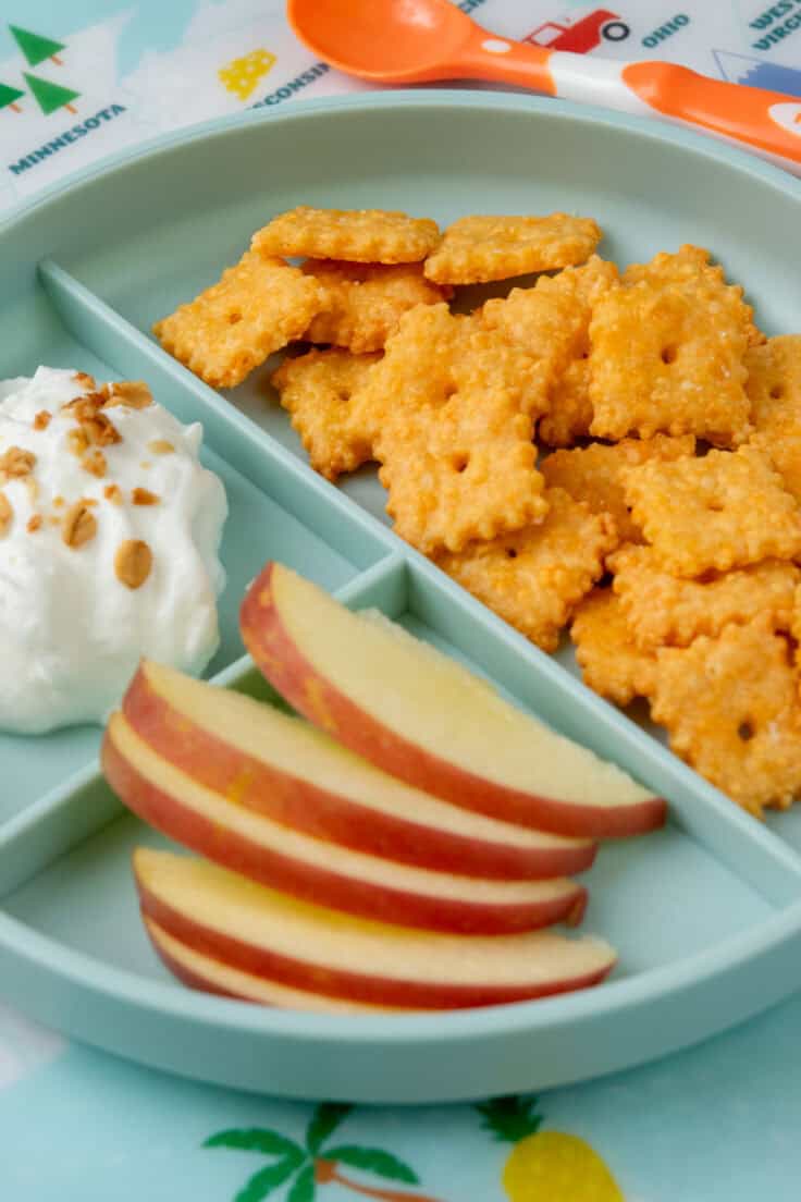 Divided snack plate with homemade Cheez-Its, sliced apples, and creamy yogurt topped with crunchy granola for an easy snack.