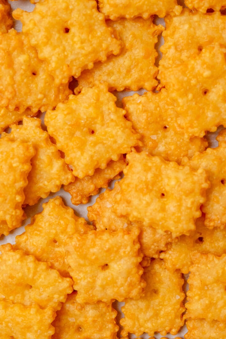 Close-up overhead view of homemade Cheez-Its with crisp golden edges, flaky sea salt, and a signature hole in the center of each cracker.