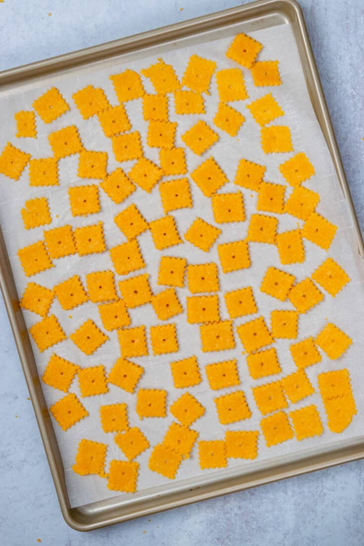 Homemade cheez-its spread out on a baking sheet, ready to be baked.