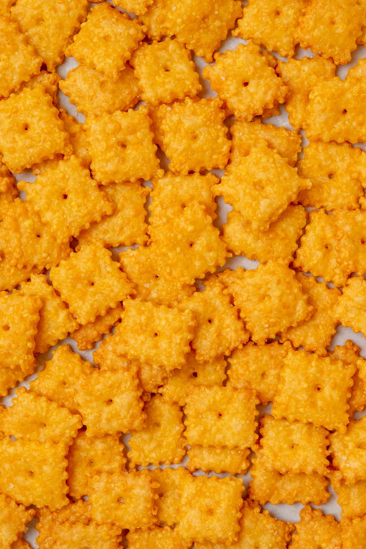 Overhead view of crispy homemade Cheez-Its baked until golden, with a hole in the center of each cracker and a sprinkle of flaky sea salt on top.