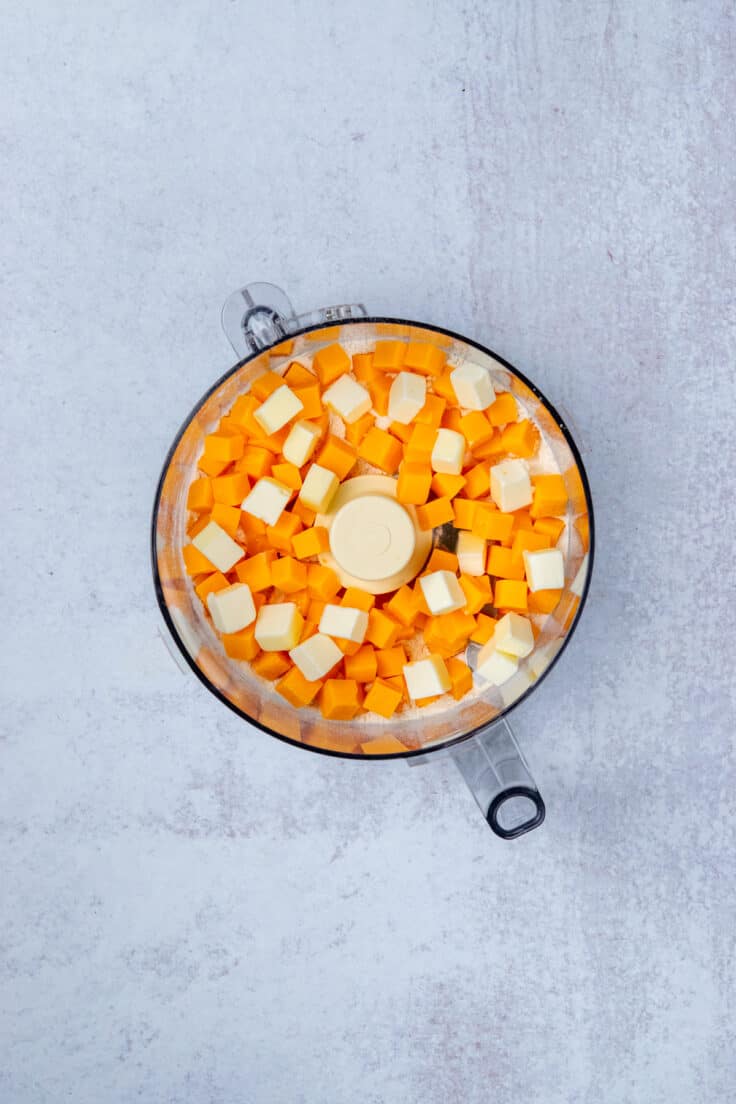 Cold sharp cheddar and butter cubes added to flour mixture in food processor bowl before being pulsed.