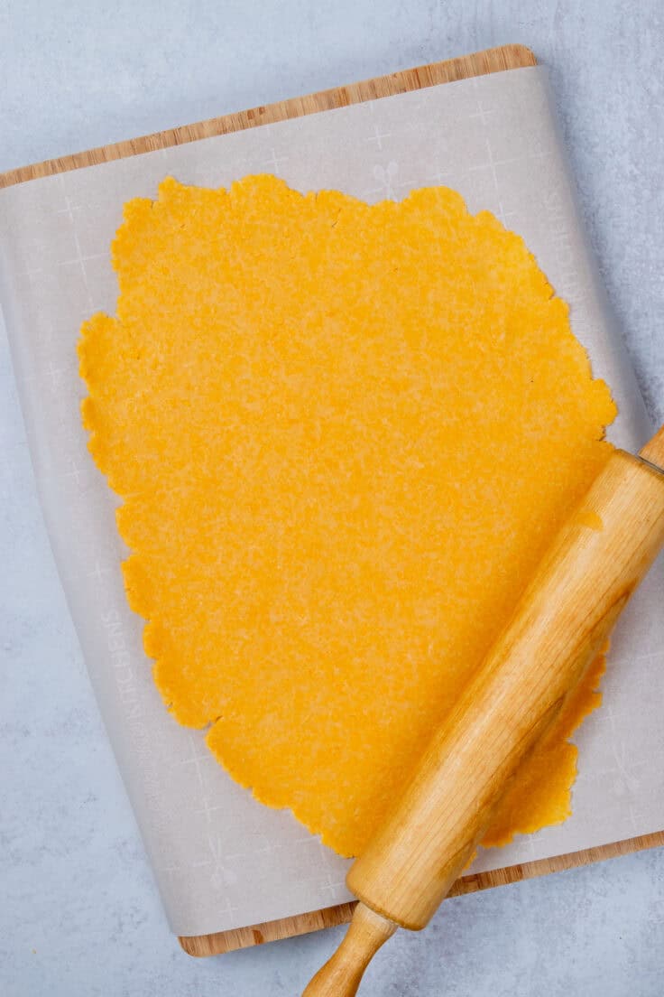 Homemade Cheez-Its dough rolled into a thin rectangle on parchment paper.