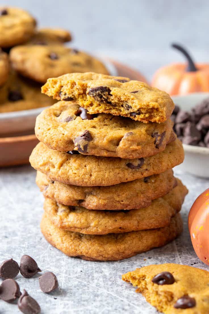 A stack of pumpkin chocolate chip cookies with the top cookie broken open to reveal its crisp edges and soft, chewy center.