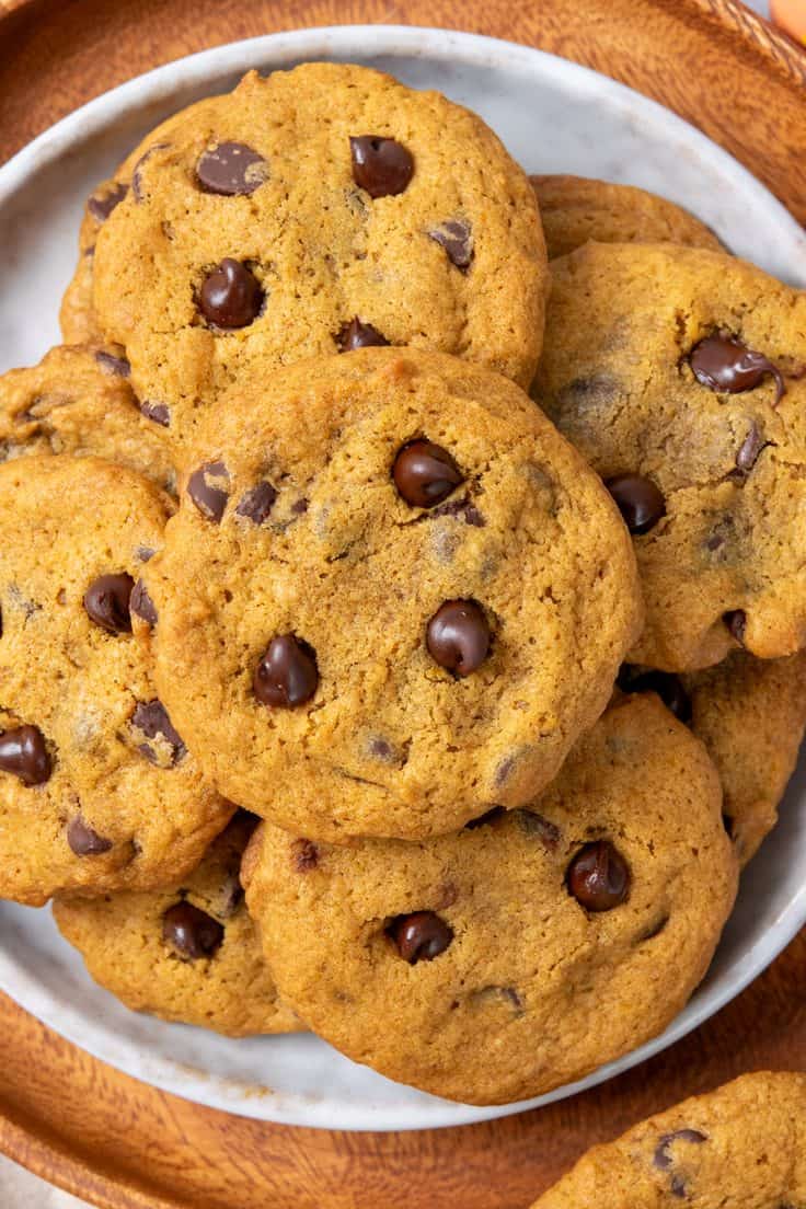 A plate piled with homemade pumpkin chocolate chip cookies topped with melted chocolate chips and showing crisp edges and chewy centers.