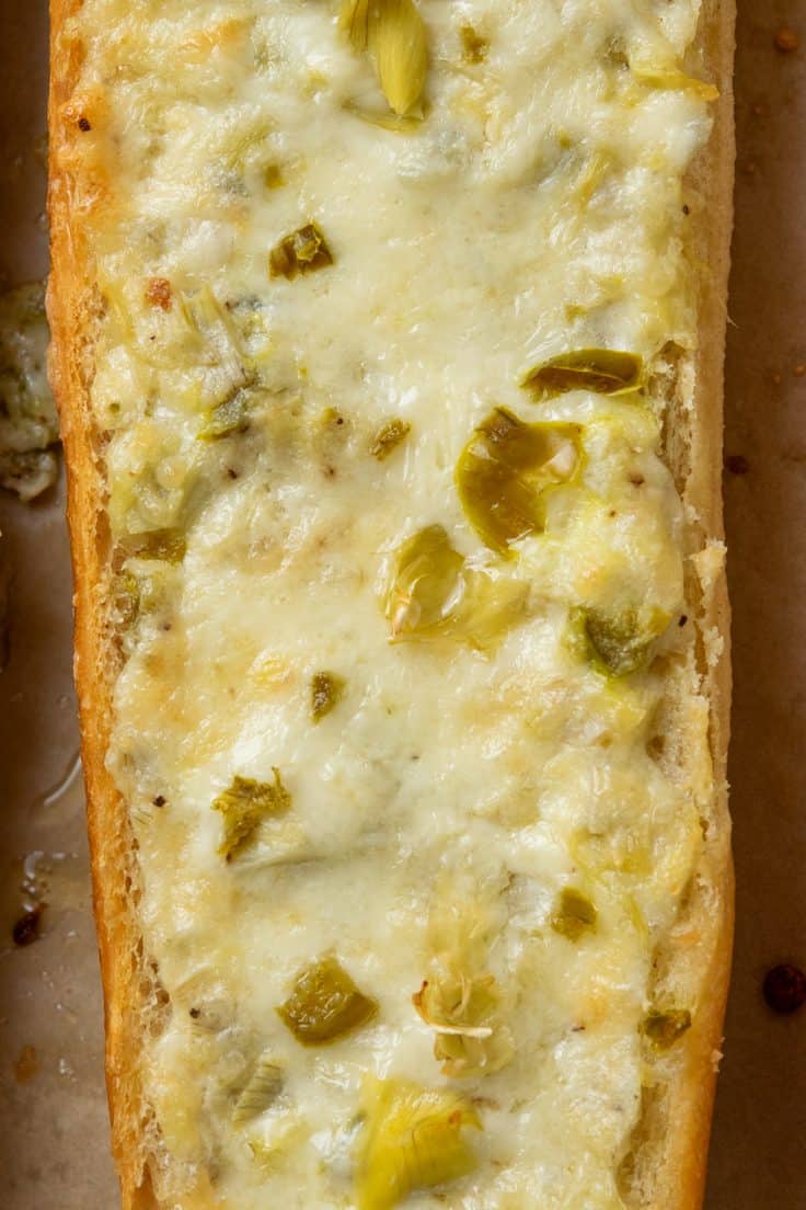 Long pieces of French bread topped with artichoke dip and melted cheese, fresh from the oven and ready to be sliced into appetizer pieces.