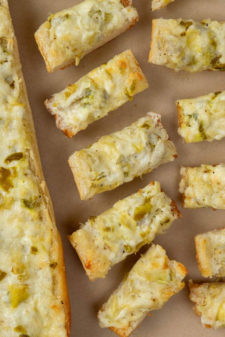 Artichoke bread on a baking tray, showing one long piece of French bread alongside pieces sliced into two-inch portions for serving.
