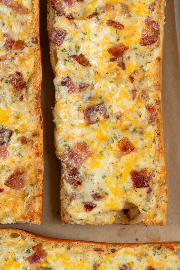 Overhead close-up of freshly baked bacon ranch cheese bread on a parchment-lined baking sheet, showing the hot, gooey melted cheese before slicing.