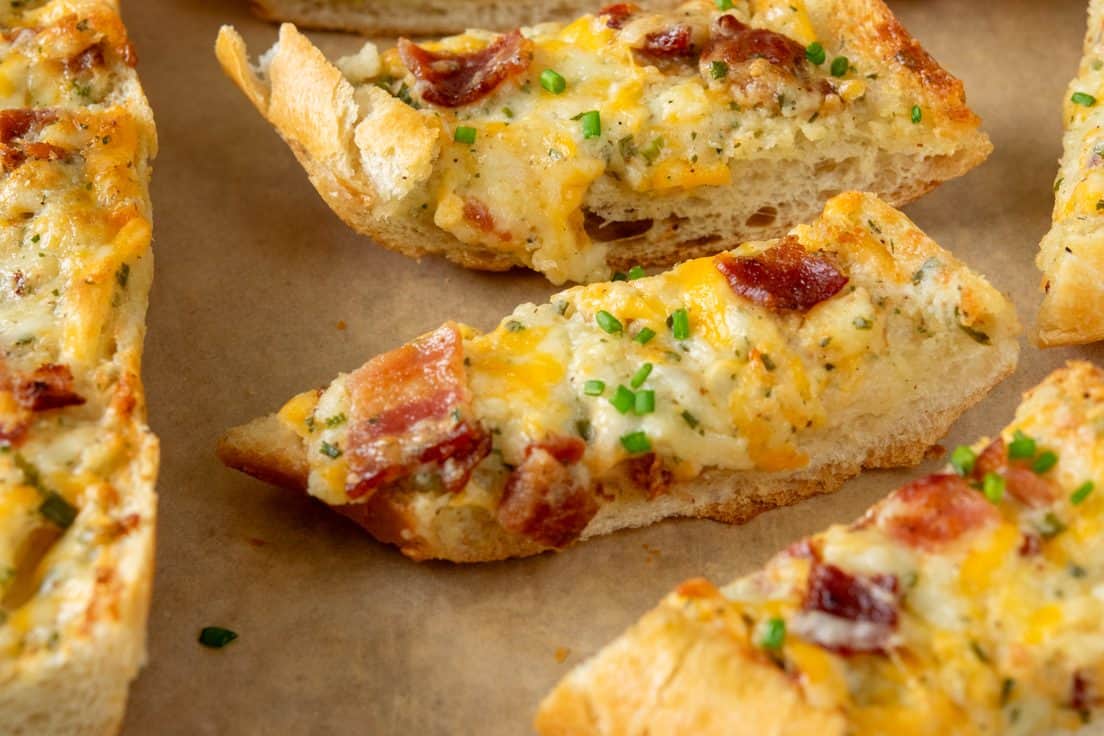 Close-up of bacon ranch cheese bread with golden edges, melted cheese dripping down the side, and bacon scattered across the cheesy topping.