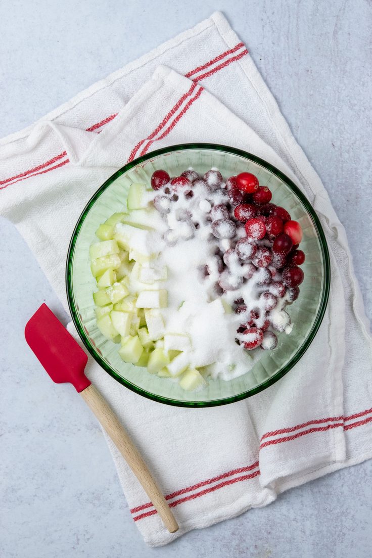 Chopped apples, cranberries and sugar in a mixing bowl for apple cranberry crisp.