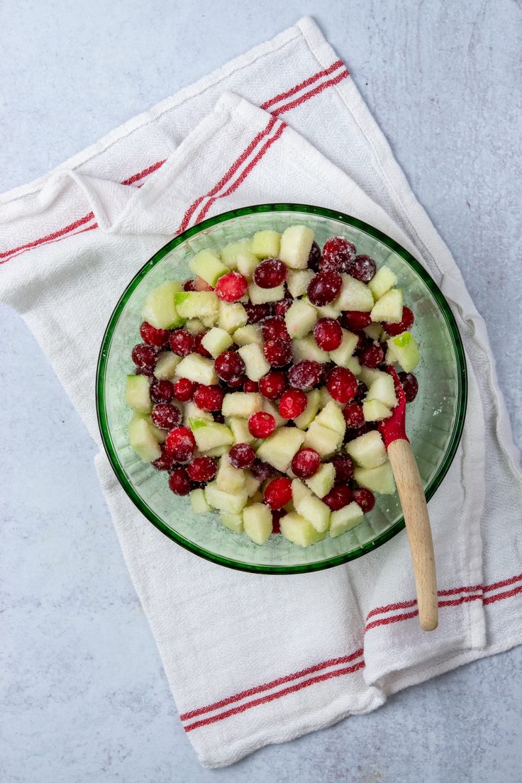 Chopped green apples and whole cranberries mixed with sugar and flour in a bowl before baking.