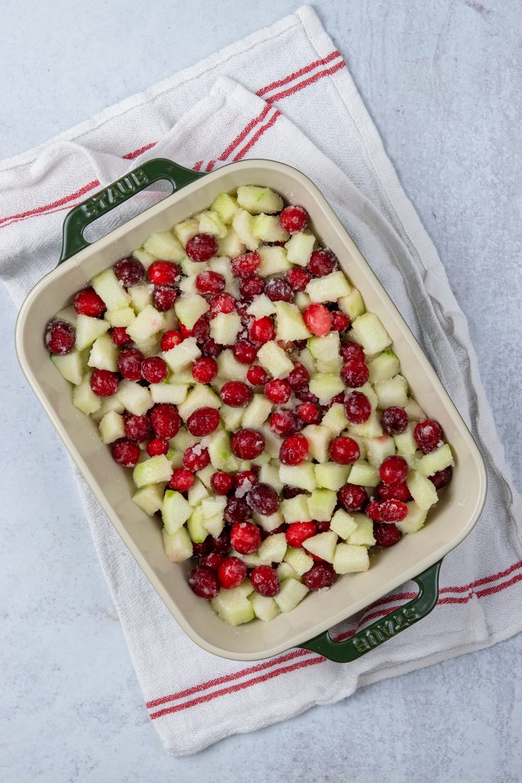 Sweetened apples and cranberries spread in a baking dish for making apple cranberry crisp.
