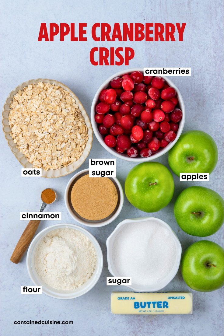 An overhead view of the ingredients for apple cranberry crisp, including fresh cranberries, Granny Smith apples, oats, brown sugar, flour, cinnamon, butter, and granulated sugar, arranged in labeled bowls.