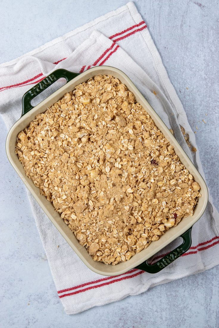 Apple and cranberry filling covered with an even layer of buttery brown sugar oat crumble in a baking dish.