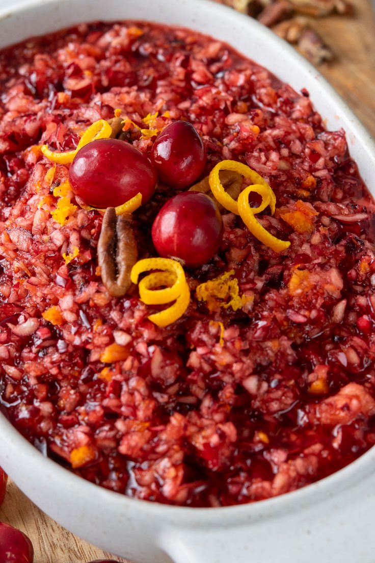 A serving dish of homemade cranberry relish garnished with three fresh cranberries, chopped pecans, and orange zest, ready to serve alongside Thanksgiving dinner.