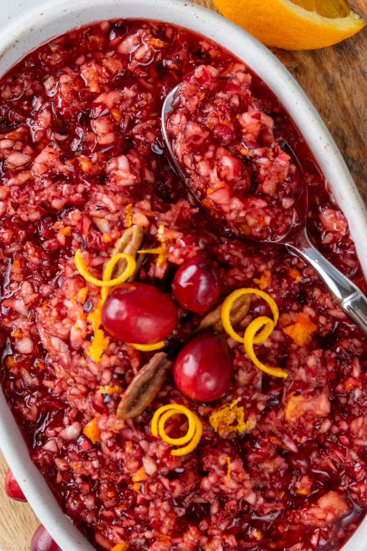 A spoon scooping chunky homemade cranberry relish from a serving bowl, showing the juicy mixture of fresh cranberries, apple, and orange.
