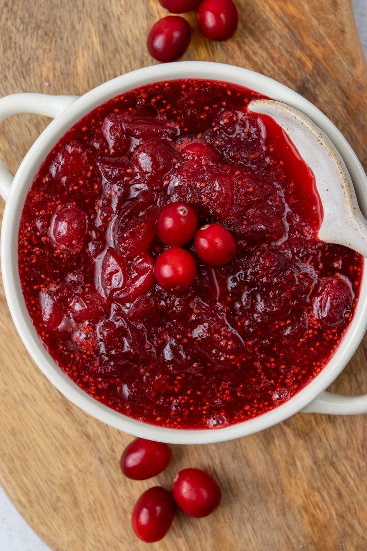Overhead view of thick homemade cranberry orange sauce in a serving bowl with a decorative spoon and three whole cranberries in the center, ready to serve with Thanksgiving or Christmas dinner.