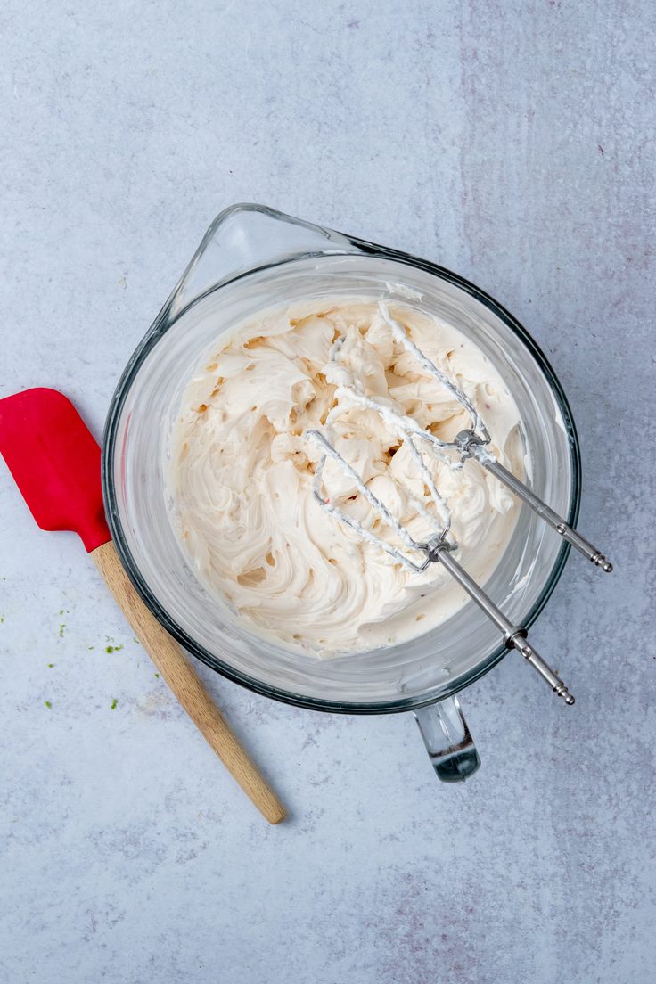 A mixing bowl with beaters resting in smooth whipped cream cheese and sour cream, showing the creamy, spreadable base for cranberry jalapeno cream cheese dip.