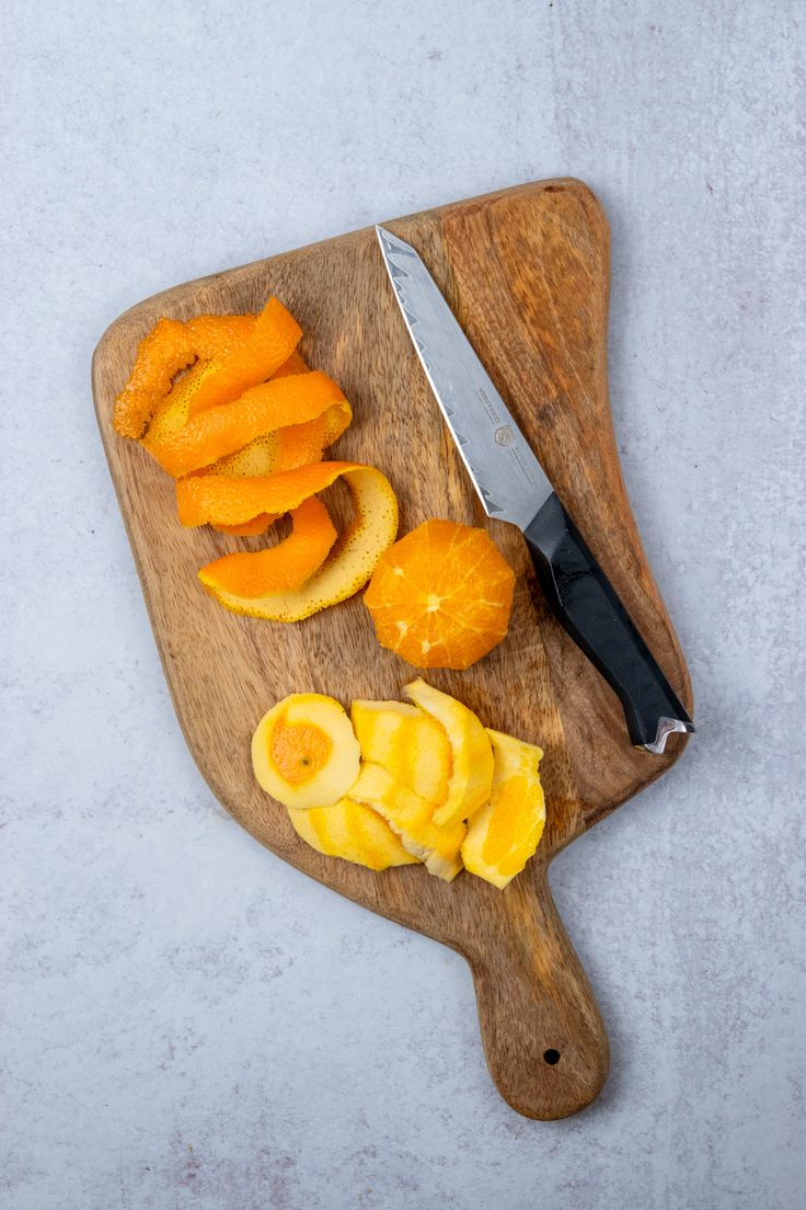 An orange on a cutting board with the peel removed and the bitter white pith trimmed away, showing how to prepare fresh orange for homemade cranberry relish.